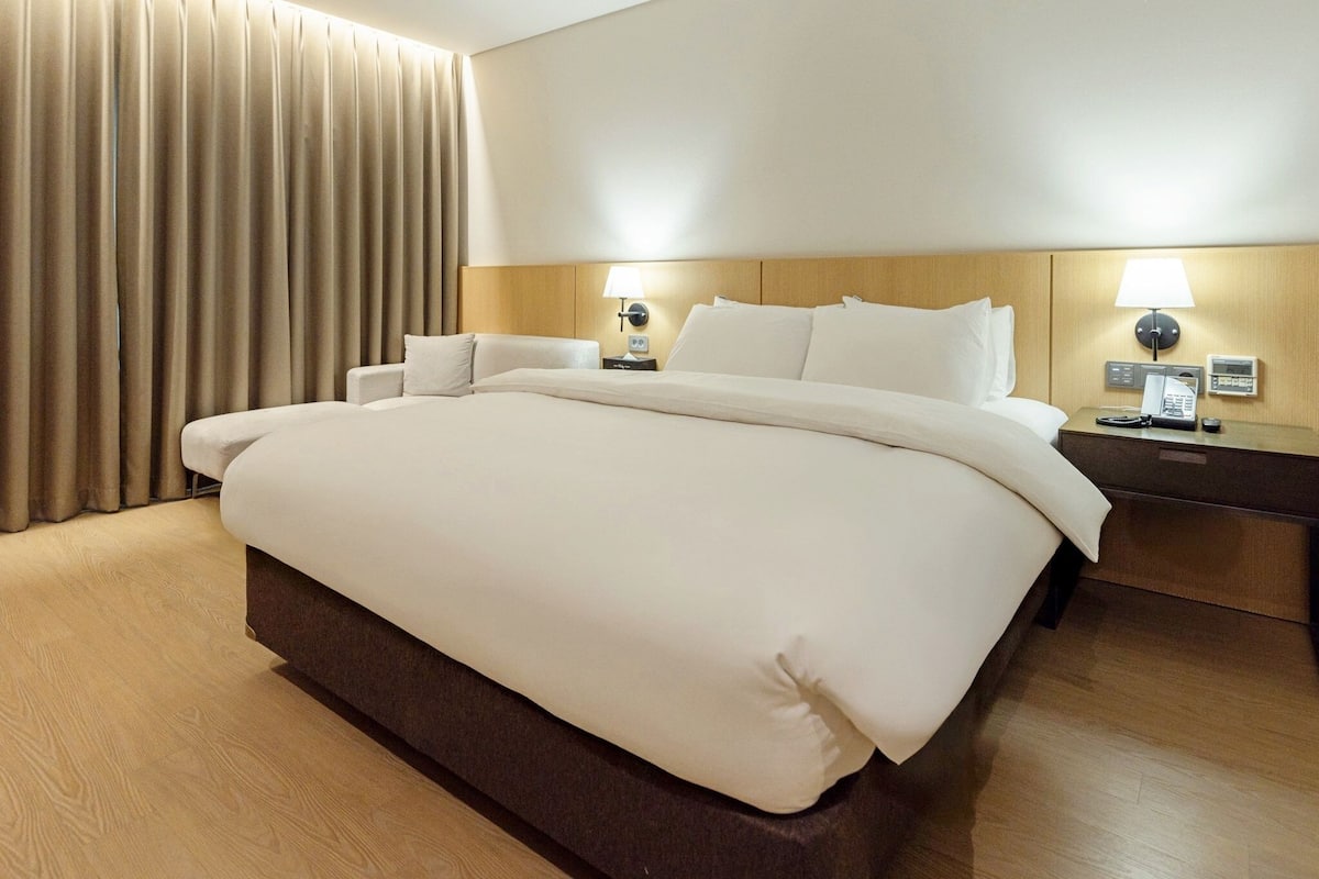 Una habitación de hotel con una cama grande, dos mesitas de noche, una lámpara y una cortina.