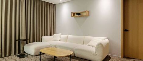 A modern living room with a sectional sofa, a small round table, a wall-mounted TV, and a door.