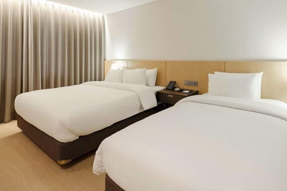 Una habitación de hotel con dos camas, un cabecero de madera, una mesita de noche con un teléfono y una cortina.
