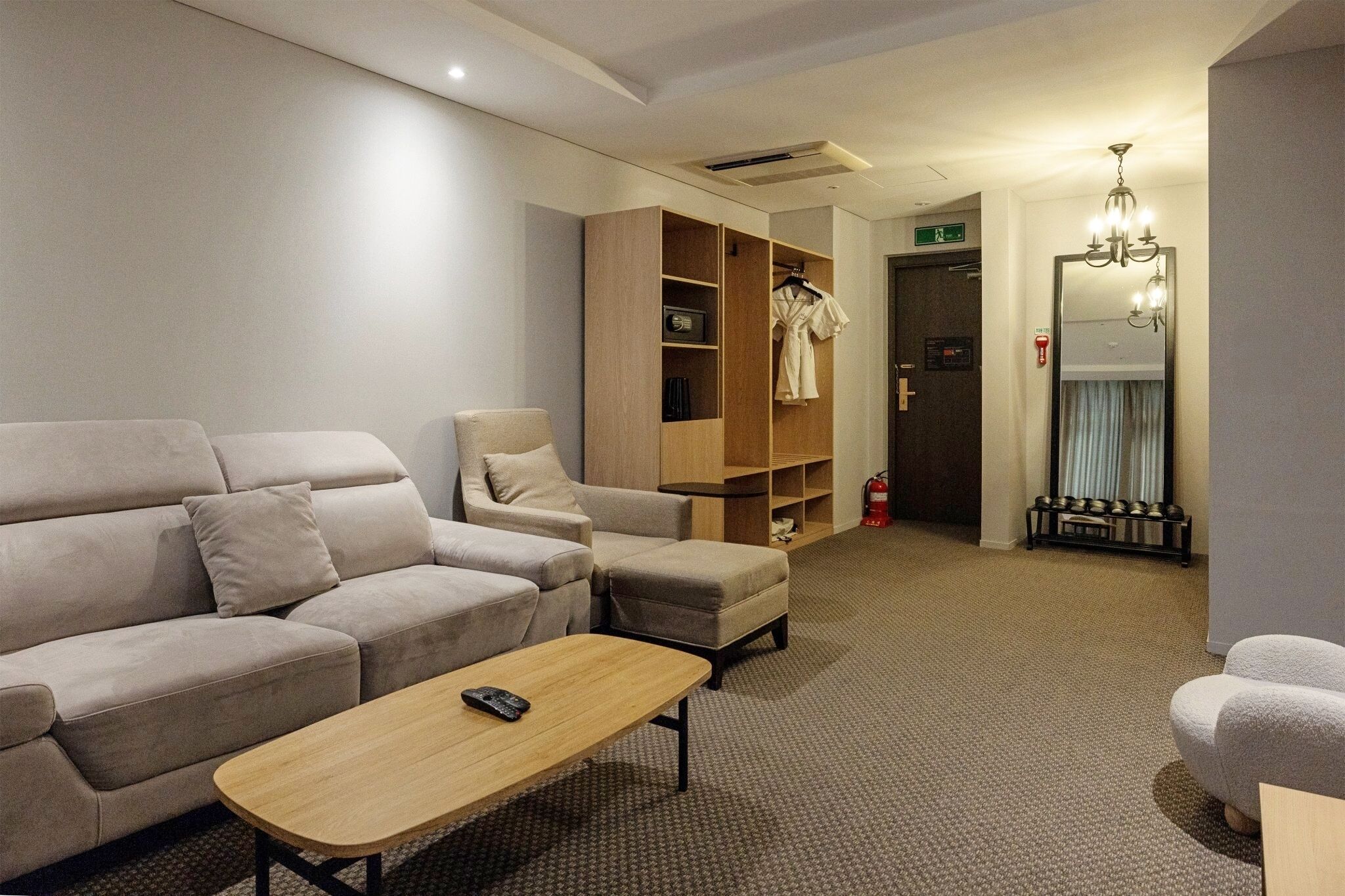 Una habitación de hotel moderna con sofá, sillón y un mueble de madera con una bata colgada.