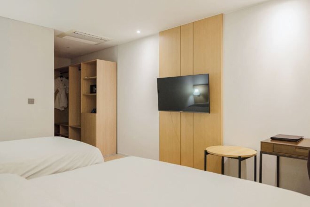 Et moderne hotelværelse med seng, fjernsyn ophængt på væggen, et lille bord og et skab.