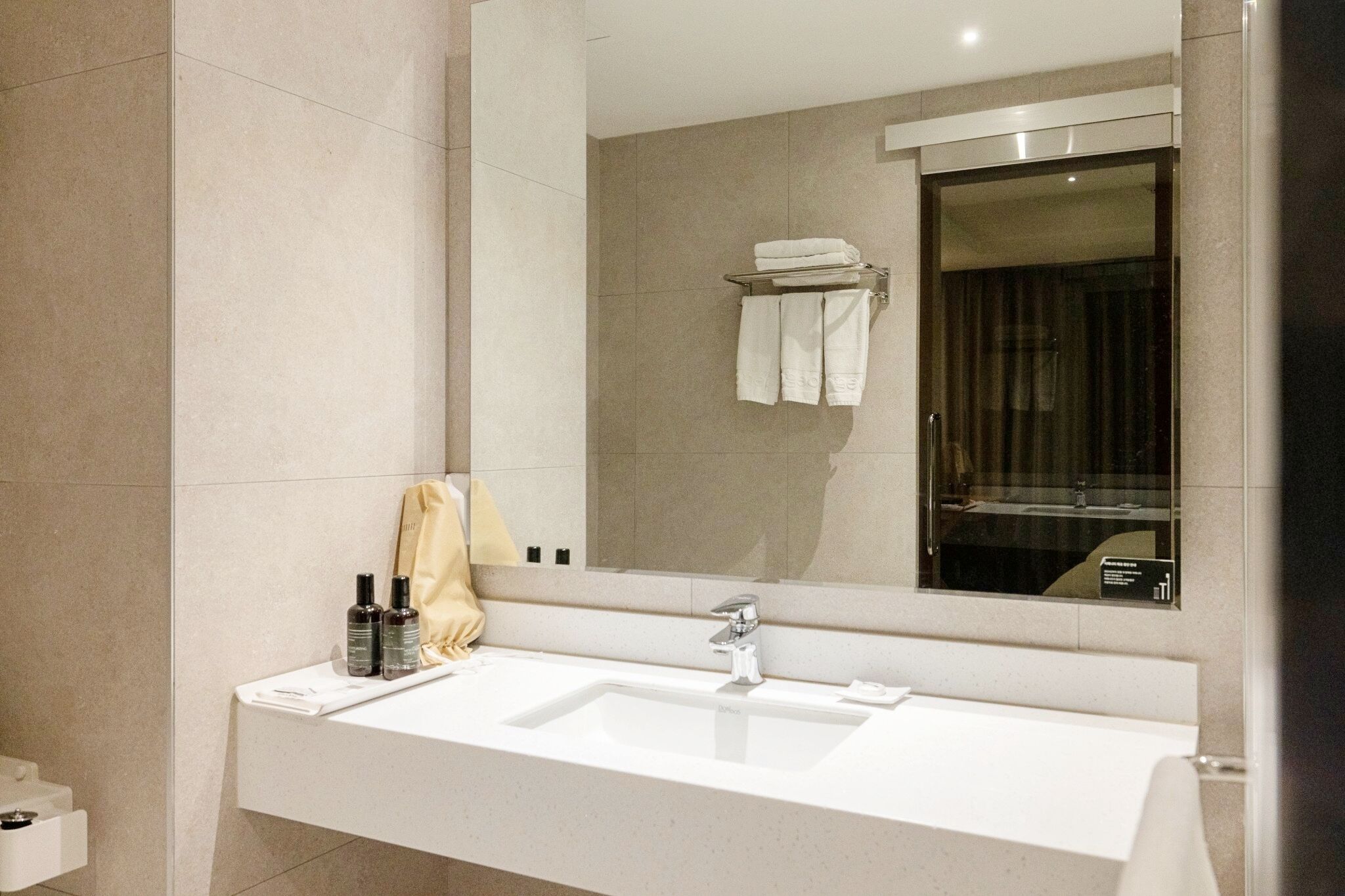 A modern bathroom with a large mirror, a white sink, and a towel rack.
