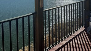 A wooden deck with a railing overlooking a lake, a hanging light fixture, and a clear sky.