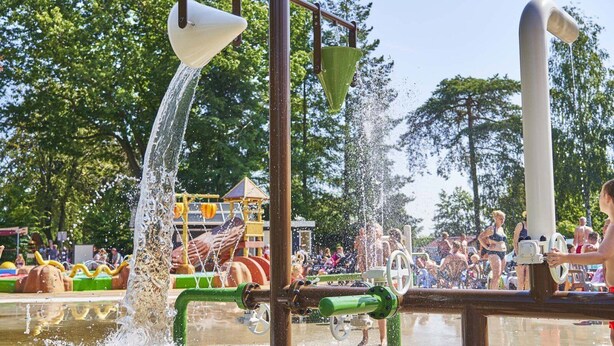 A water play area with multiple water jets and a playground in the background. - Forest Family Home - 6 Persoons op 5 Sterren Park (Beekbergen)
