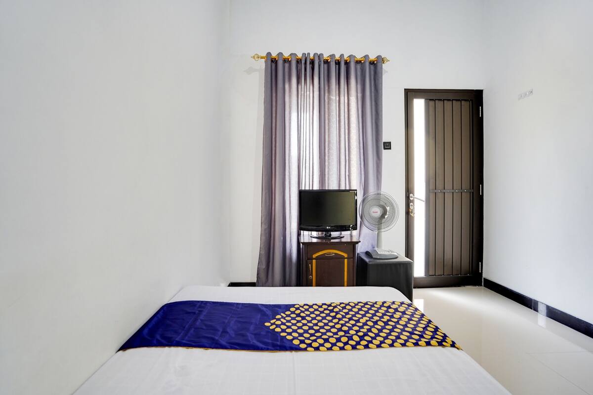 Una habitación de hotel con cama, televisor, ventilador y puerta con cortina.