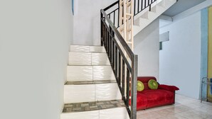 Una escalera con peldaños blancos y estampados, un sofá rojo con cojines verdes y una barandilla de metal.