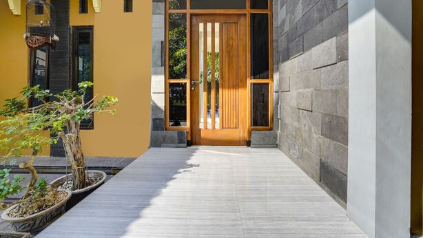 Una entrada moderna a un edificio con puerta de madera, paredes de piedra y una planta en maceta.
