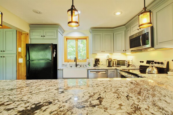 A kitchen with a granite countertop, stainless steel appliances, and light green cabinetry.