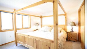 Ein hölzernes Himmelbett mit Nachttisch und Lampe, einem Schminktisch und einem Fenster.