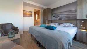 Ein modernes Schlafzimmer mit einem großen Bett, einem Holzkopfende, einer Sitzecke mit einem Sessel und einem kleinen Tisch mit einer Glasvase.