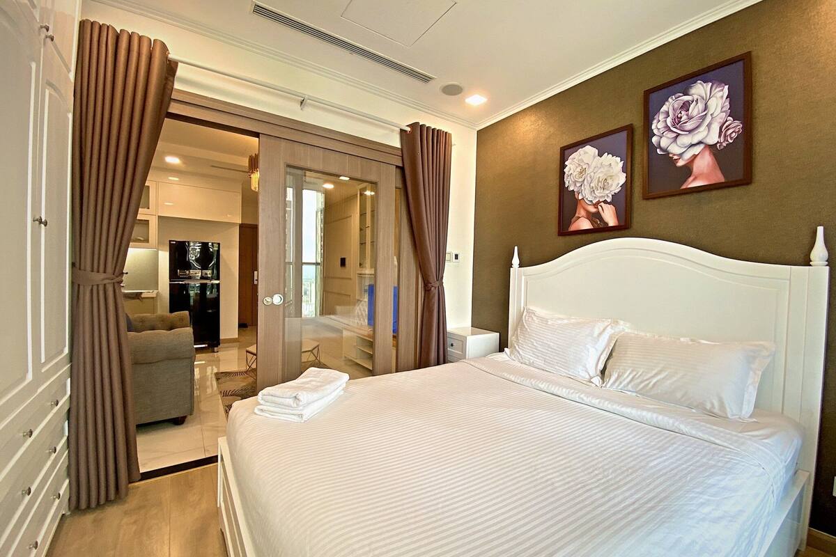 Une chambre d’hôtel avec un grand lit, un canapé et une télévision. Il y a des rideaux aux fenêtres et un tableau au mur.