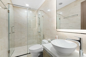 Une salle de bain moderne avec une douche à parois de verre, des toilettes blanches et un grand lavabo blanc.