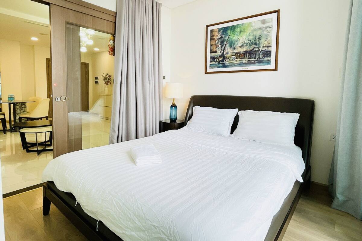 Une chambre d’hôtel avec un grand lit, un bureau avec une chaise, un tableau au mur et une vue sur le couloir.