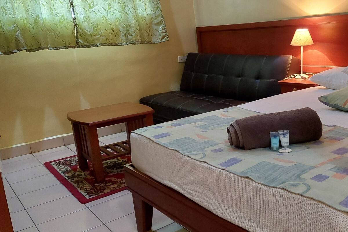 A hotel room with a bed, bedside table, lamp, and a sofa.