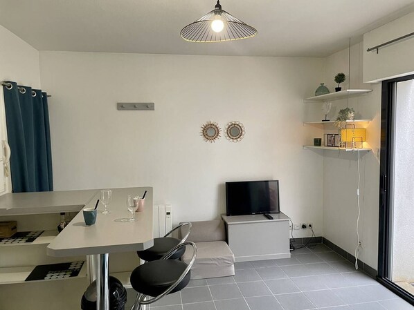 A modern kitchen with a dining area, a flat-screen TV, and a small seating space.