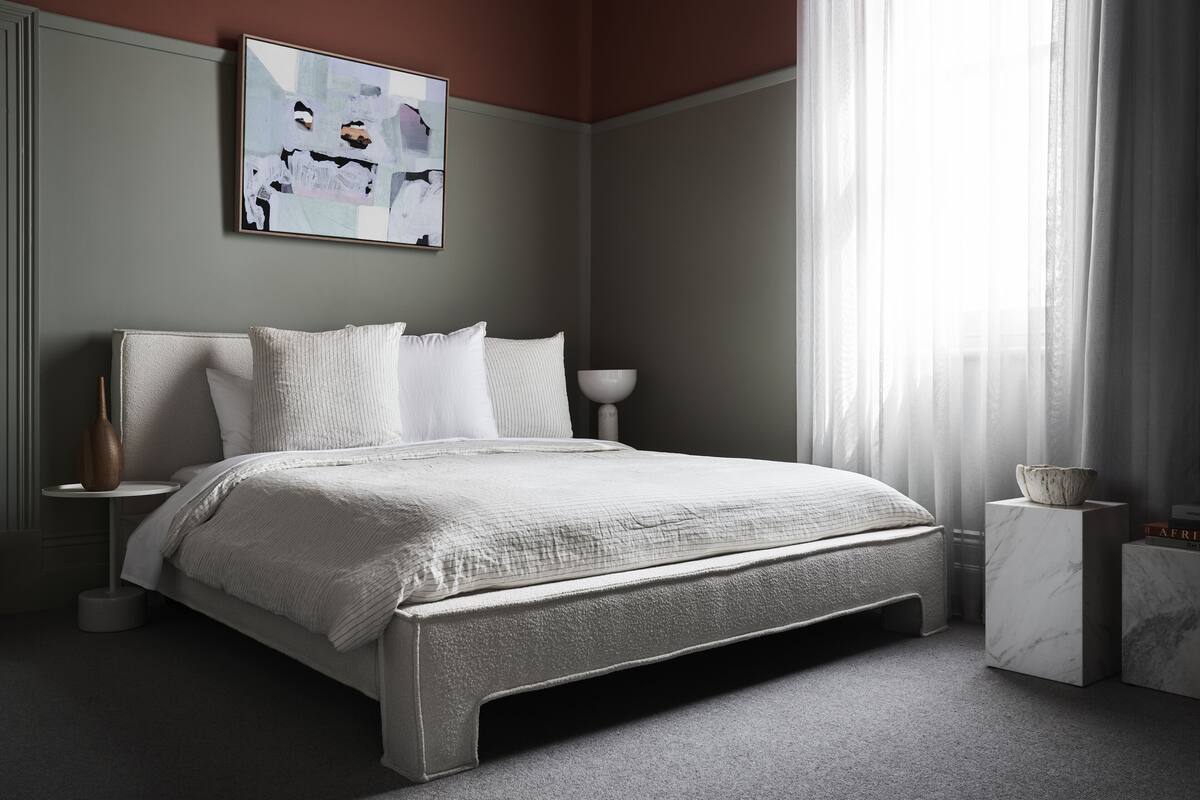 Un dormitorio moderno con una cama grande, una mesita de noche y una ventana con cortinas translúcidas.