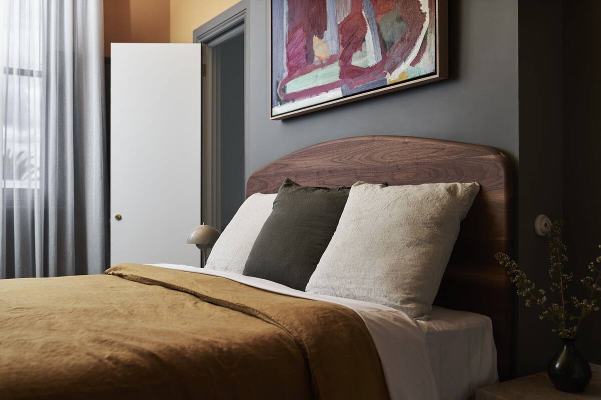 Una cama bien hecha con una manta marrón, un cabecero de madera y un cuadro en la pared superior.