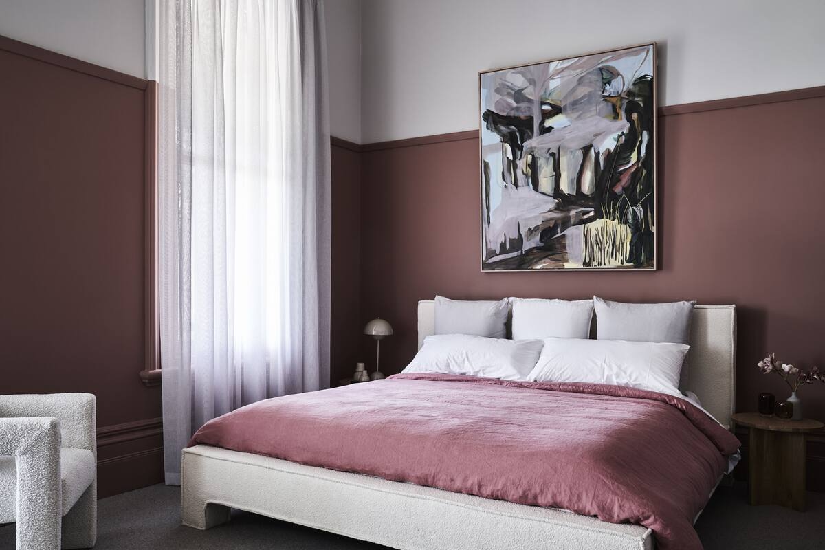 Un dormitorio con cama, mesita de noche, lámpara y un cuadro en la pared.
