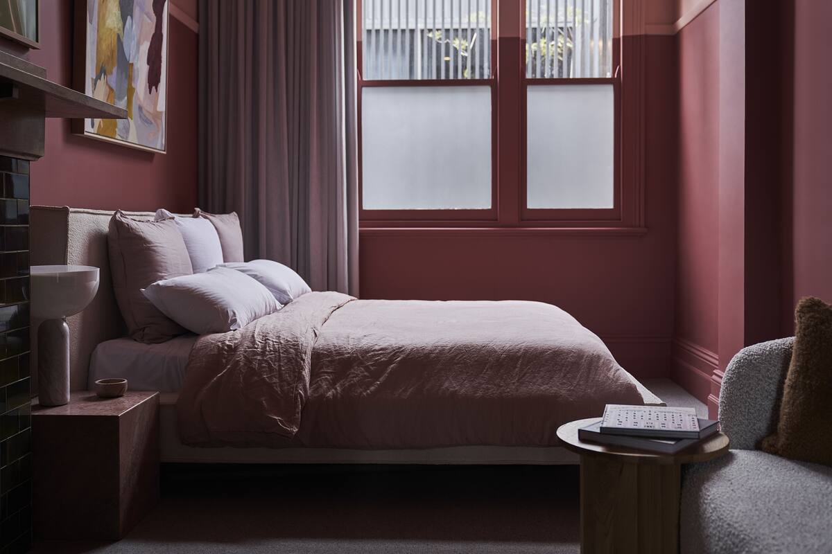 Un dormitorio con cama, mesita de noche, lámpara y ventana con cortinas.