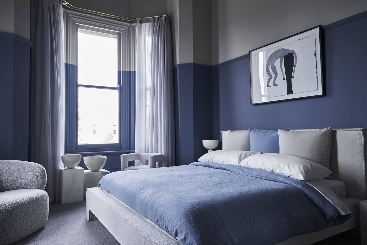 Un dormitorio moderno con una cama grande, una silla, una ventana con cortinas y una obra de arte enmarcada en la pared.