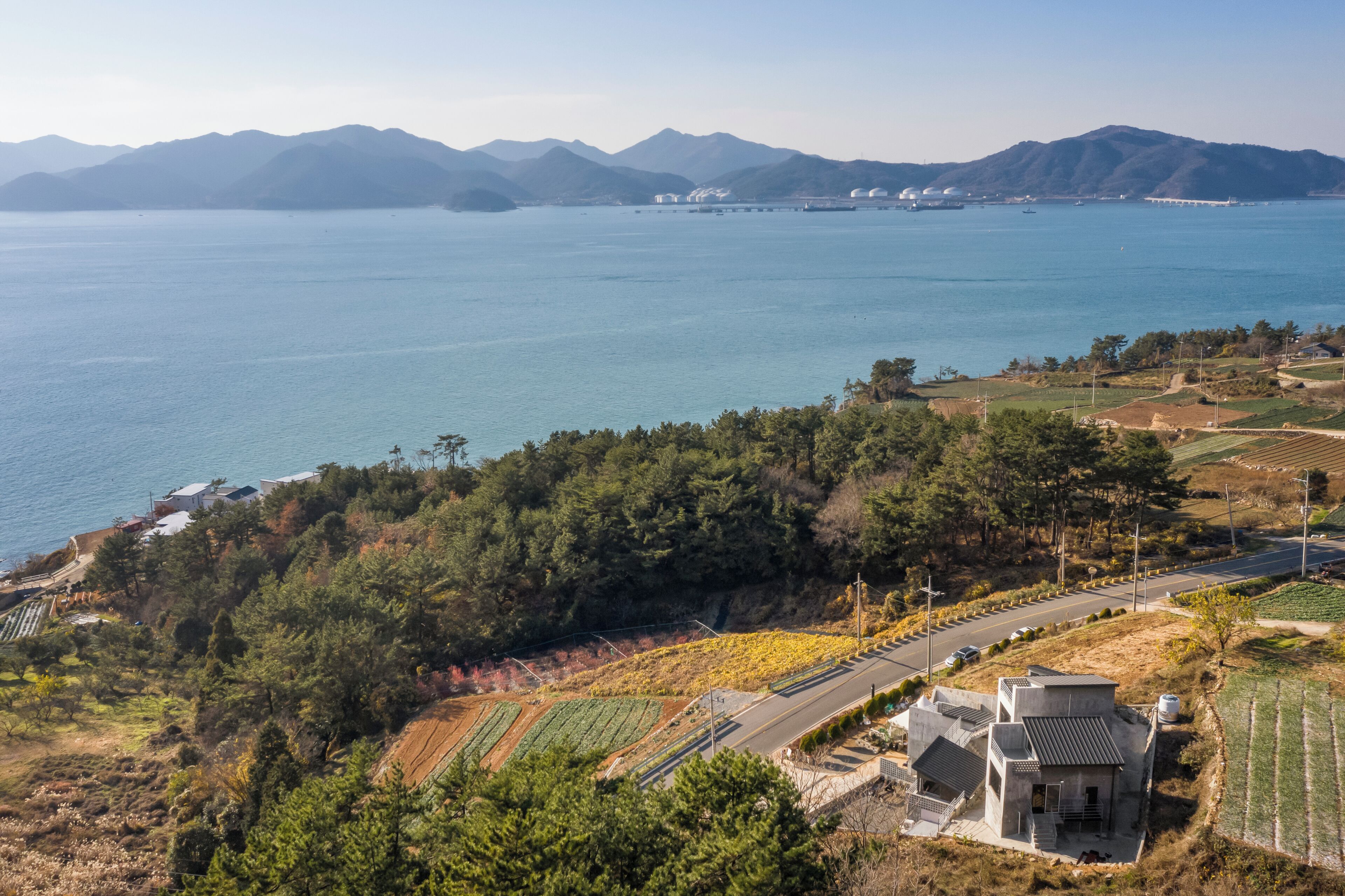 A coastal landscape with a road, buildings, and fields.