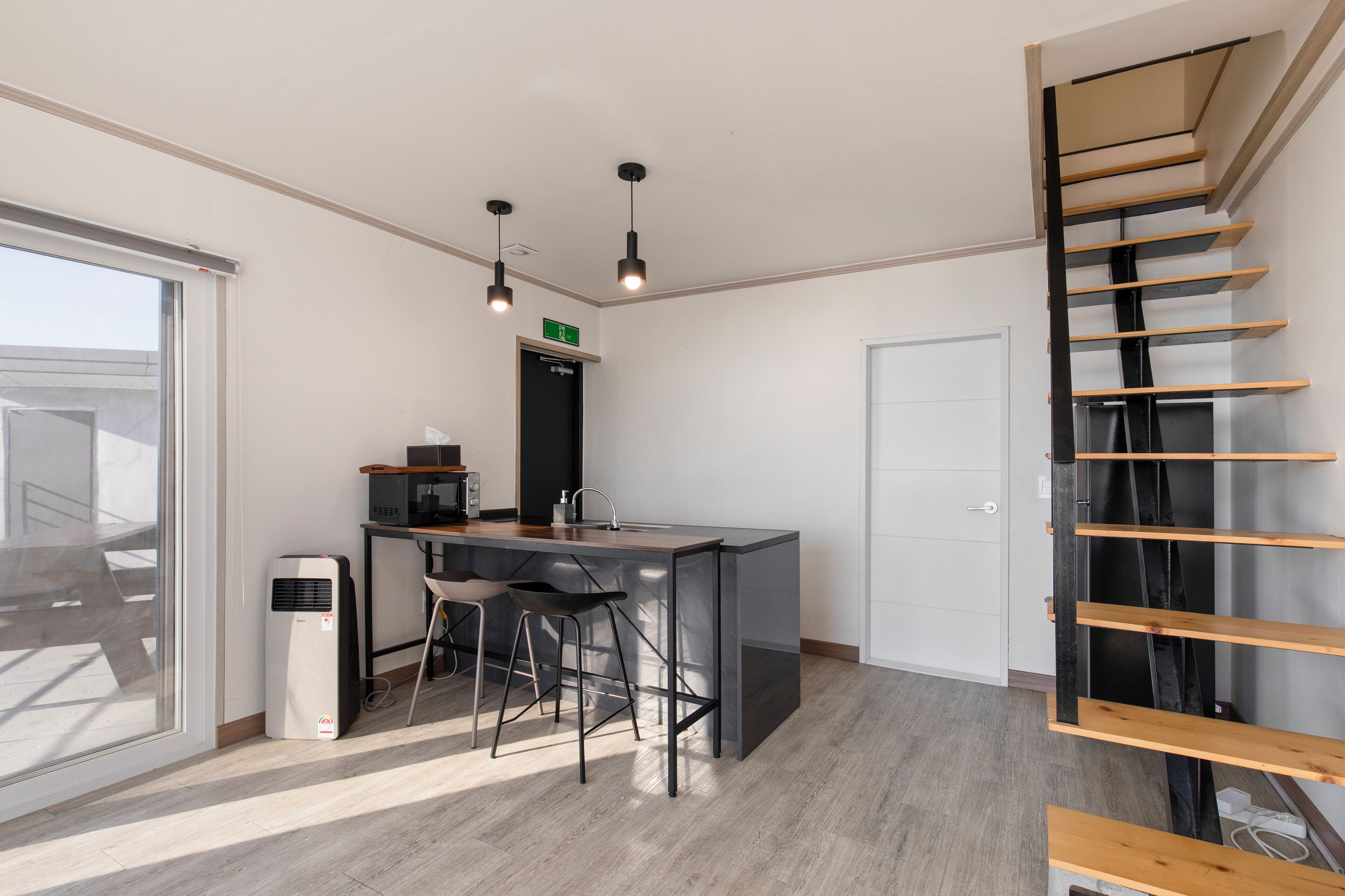 A modern kitchen with a central island, bar stools, pendant lighting, and a staircase with wooden steps.
