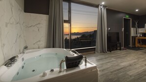 Ein modernes Badezimmer mit einer großen Badewanne, Blick auf den Sonnenuntergang durch ein großes Fenster und Holzboden.