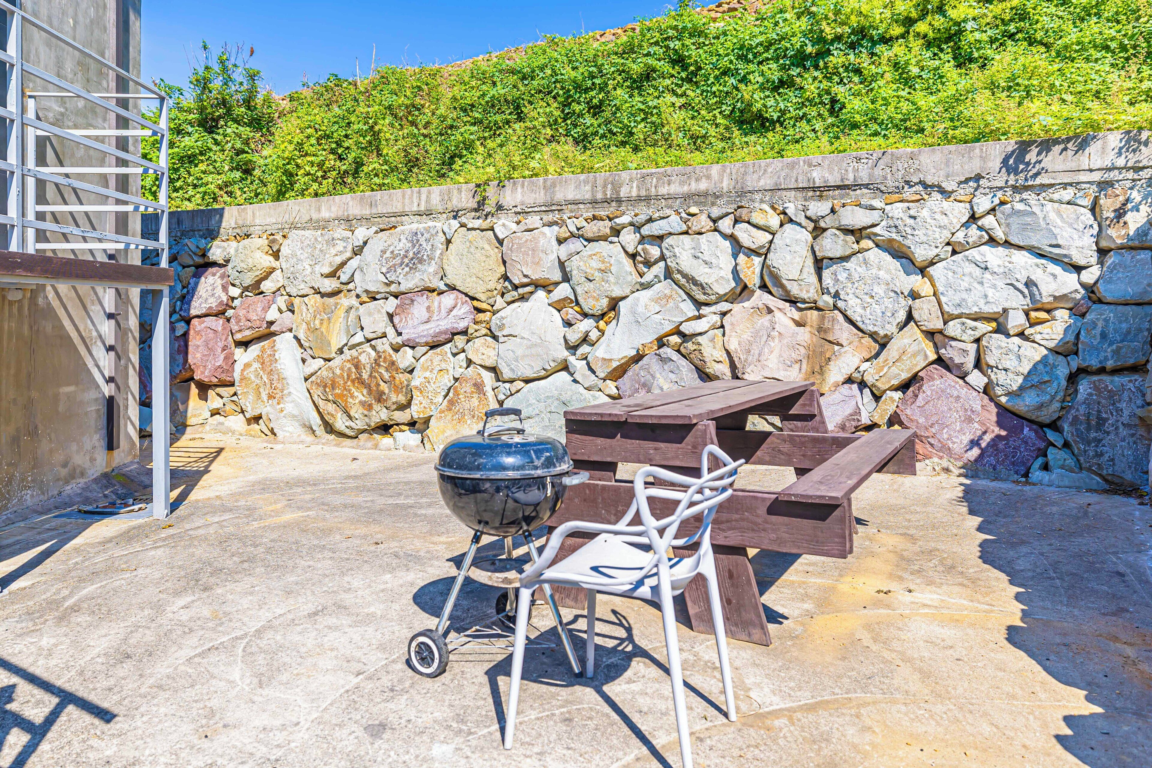 Eine Terrasse im Freien mit einer Steinmauer, einem Grill, einem Holztisch und einem Stuhl aus Metall.