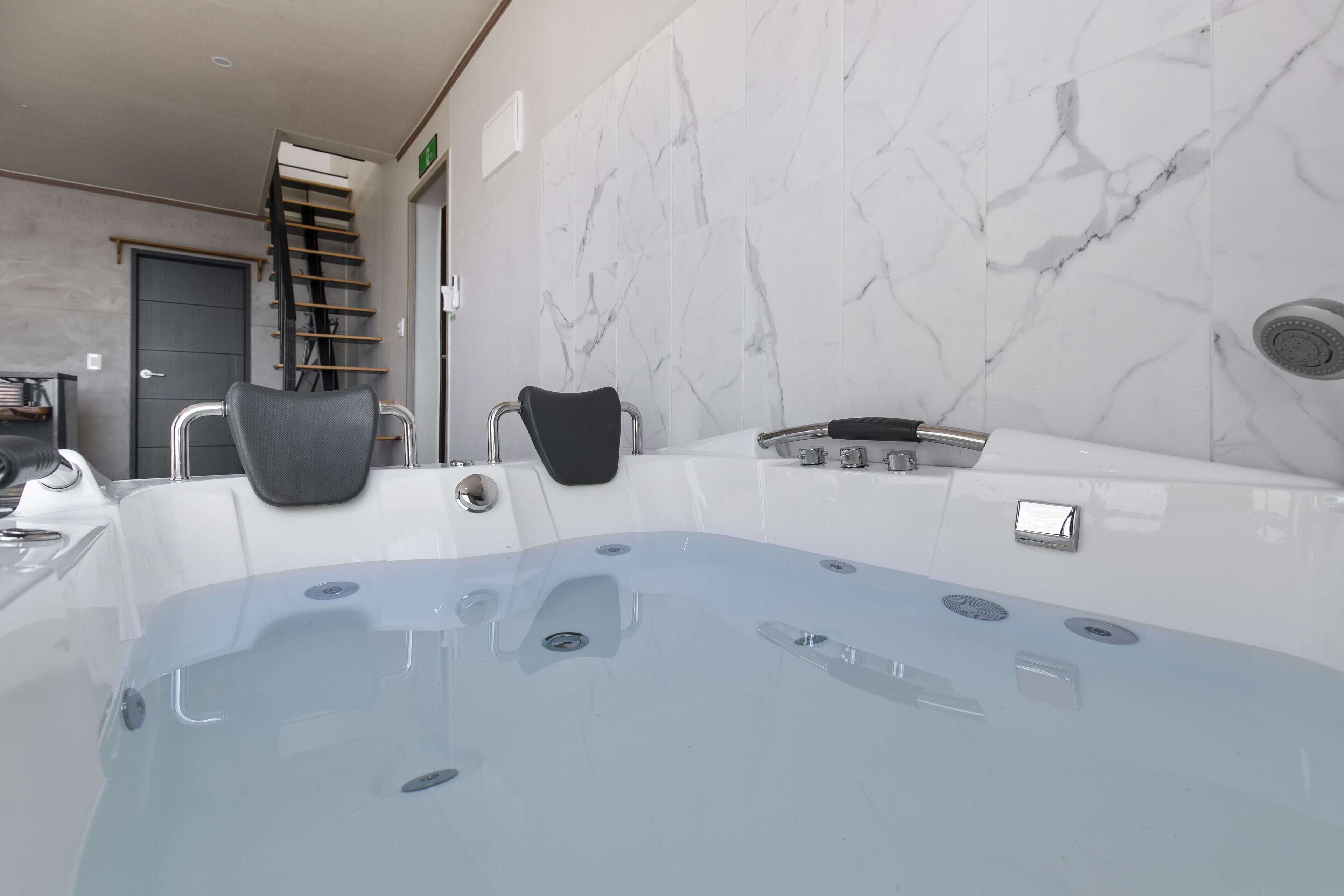 A modern bathroom with a marble wall, a bathtub, and a shower area.