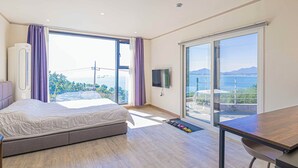 Ein modernes Schlafzimmer mit einem großen Bett, einem Fernseher und einem Balkon mit Meerblick.