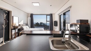 Ein modernes Hotelzimmer mit einem großen Bett, einer Küchenzeile, einem Waschbecken und Blick ins Freie.
