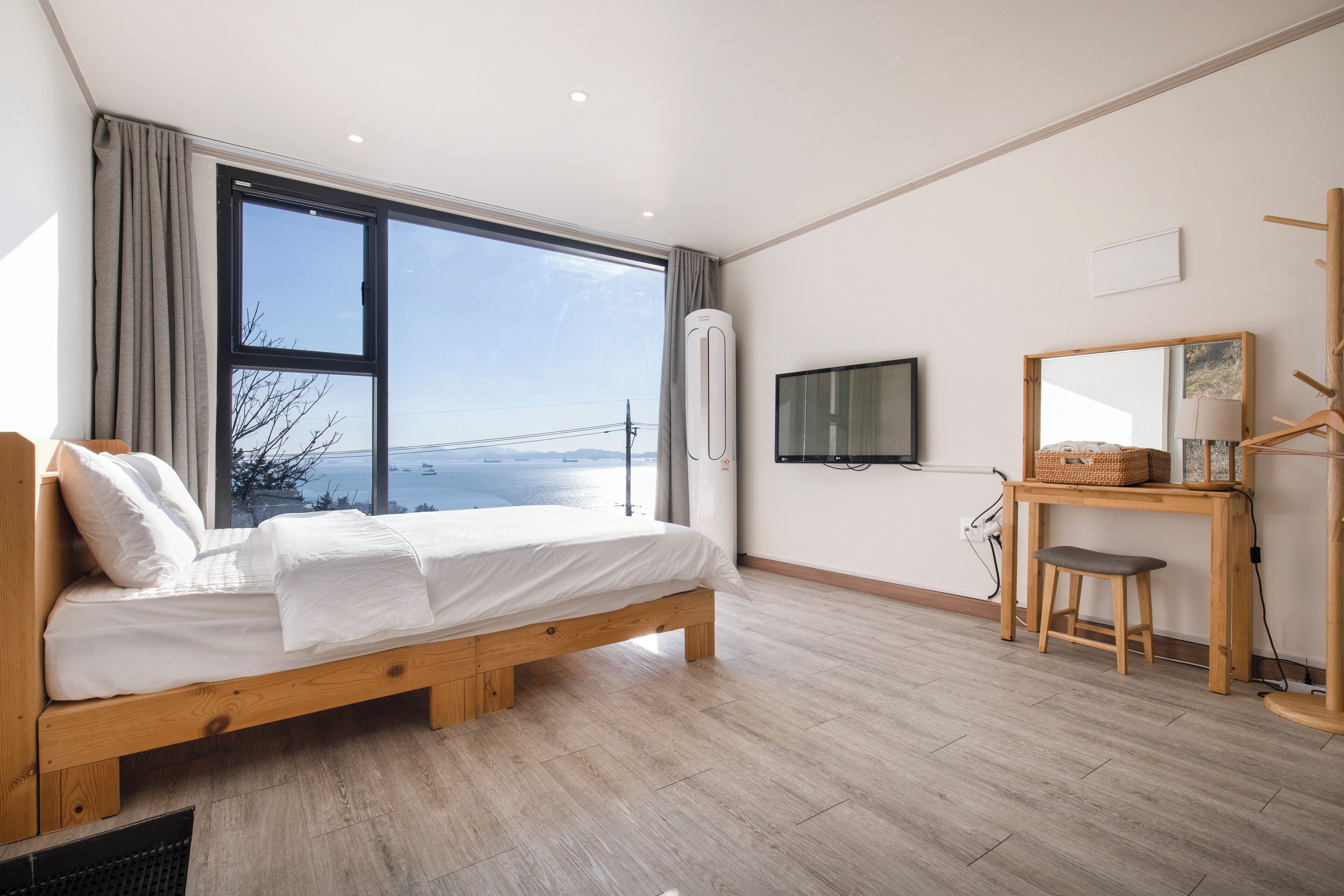 Een moderne slaapkamer met een houten bed, een groot raam, een televisie en een bureau met stoel.