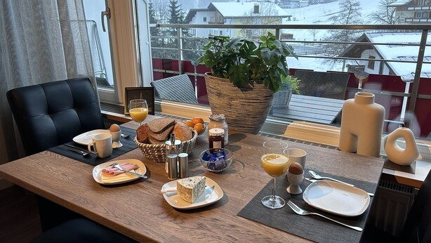 A breakfast table set with bread, eggs, and juice, overlooking a snowy mountain view. - Appartement Mittelberg in Aparthotel, Kleinwalsertal, Summer & Winter Sports

 (Mittelberg)
