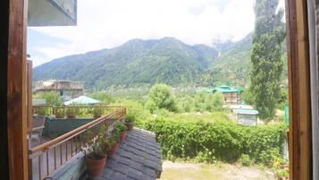 A balcony with potted plants, a view of a mountainous landscape, and a building with a green roof.