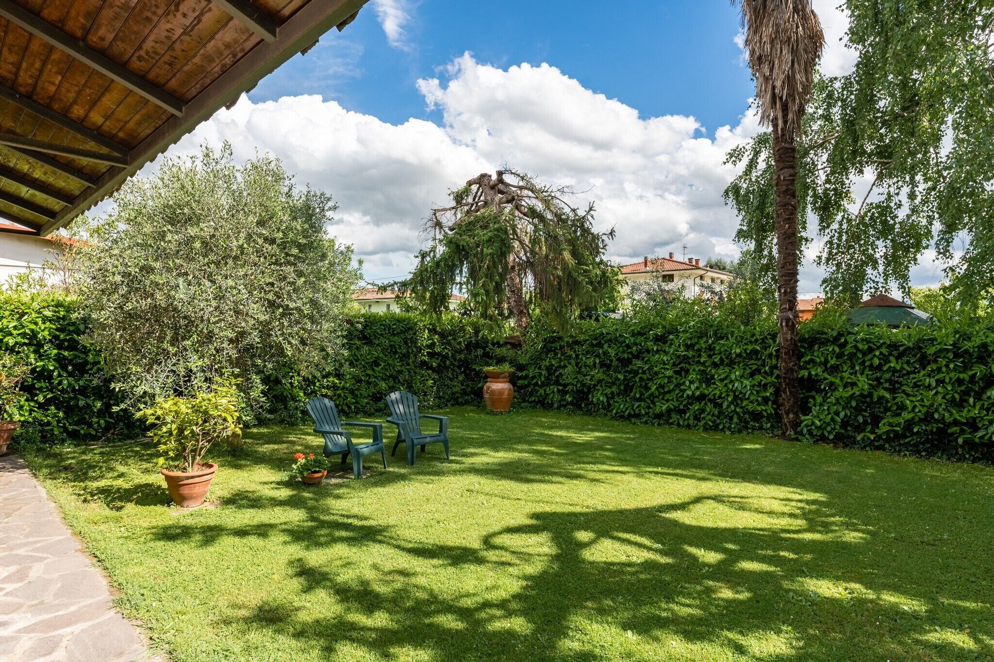 A well-maintained garden with a wooden pergola, two green chairs, and a large tree.