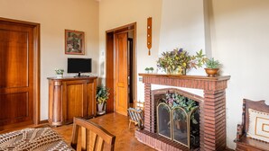 A living room with a fireplace, wooden furniture, a television, and a door. - Holiday Apartment 'Tea Rose House' with Terrace, Shared Garden & Wi-Fi (Capannori)