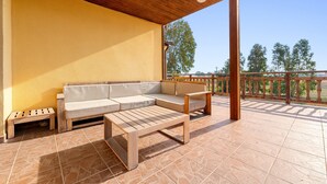 Un espacio de patio cubierto con un banco de madera, un sofá acolchado y piso de baldosas.