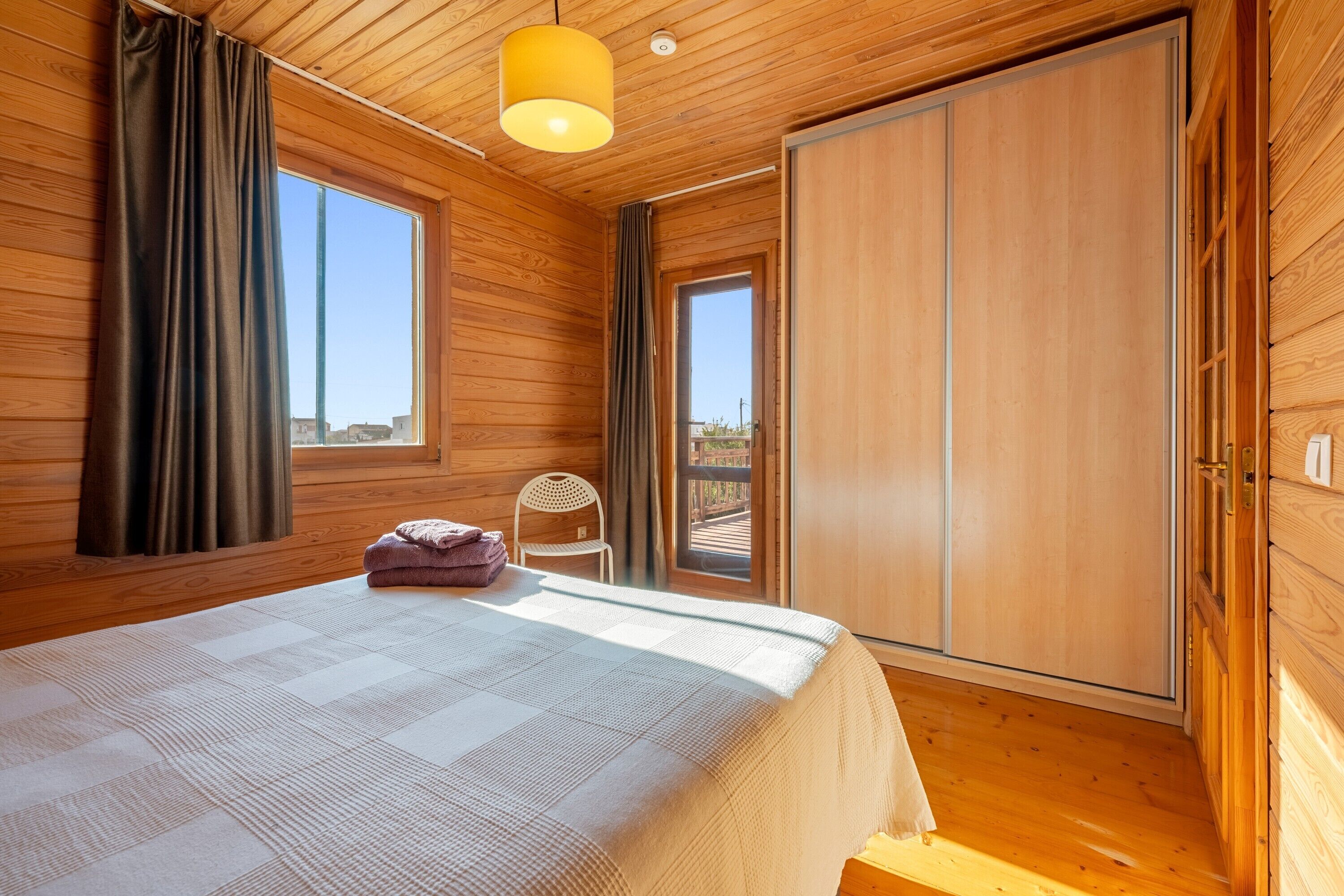 A wooden-paneled room with a bed, a chair, and a sliding door.