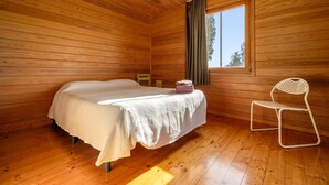Habitación de cabaña de madera con cama, una silla, un ventanal y una lámpara colgante.