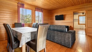 Interior de una cabaña de madera con una mesa de comedor, sillas, un sofá y un televisor.