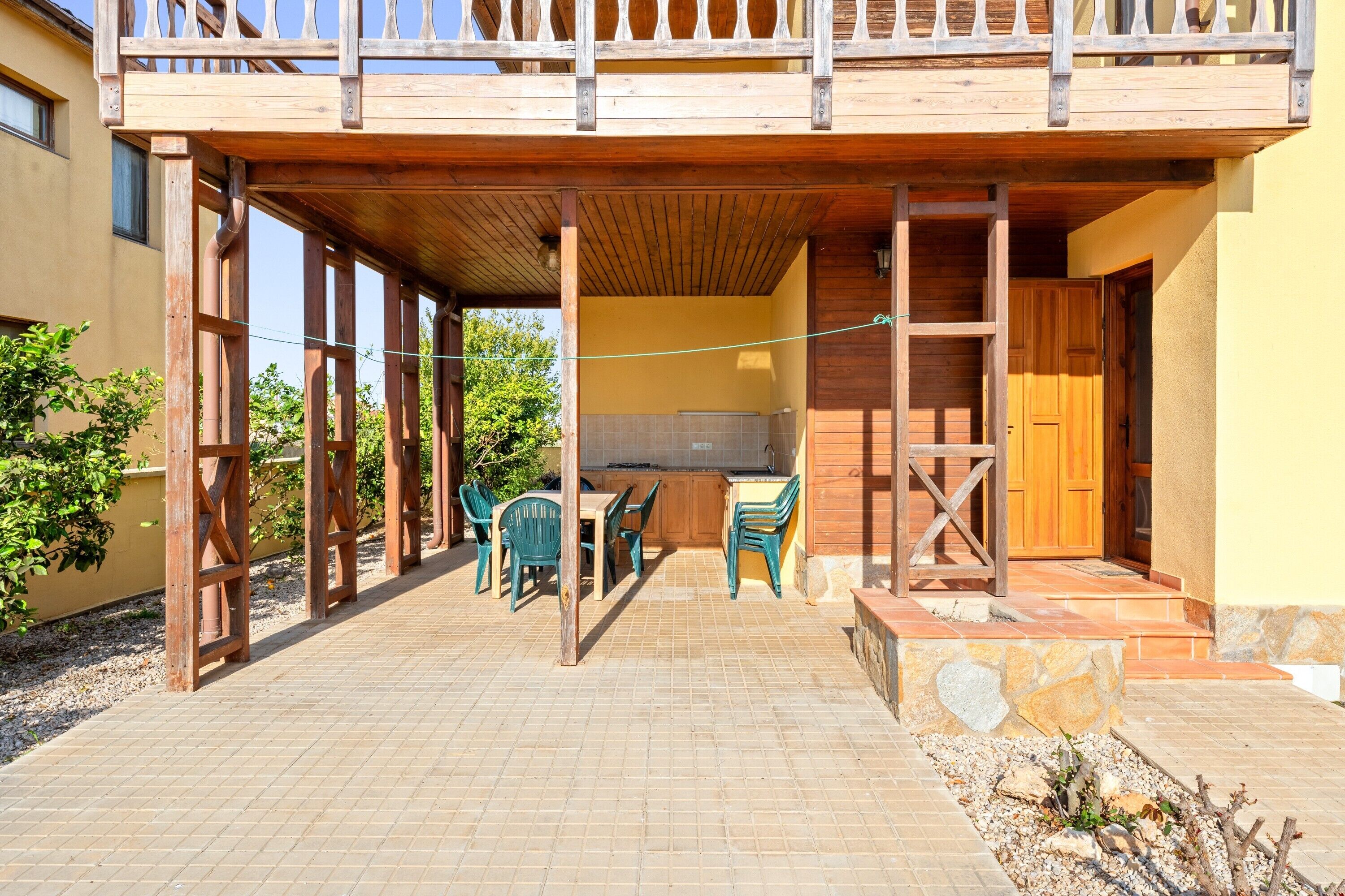 A covered outdoor area with a wooden deck, a table with chairs, and a kitchen area.