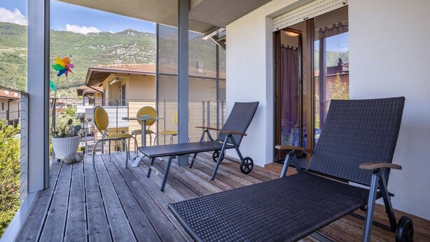A balcony with two lounge chairs, a small table, and chairs. There is a potted plant and a pinwheel decoration. - Holiday Speed Apartment with Mountain View, Private Terrace, and Wi-Fi (Arco)