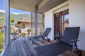 Un balcon avec deux fauteuils, une petite table et des chaises. On y trouve également un pot de fleurs et une décoration en forme de moulinet à vent.