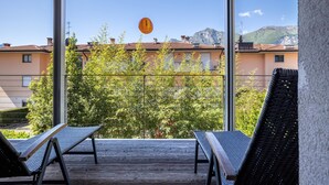 A balcony with two lounge chairs, a wooden deck, and a view of buildings and mountains. - Holiday Speed Apartment with Mountain View, Private Terrace, and Wi-Fi (Arco)