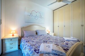 A bedroom with a bed, nightstands, a ceiling fan, a wardrobe, and a wall art piece.