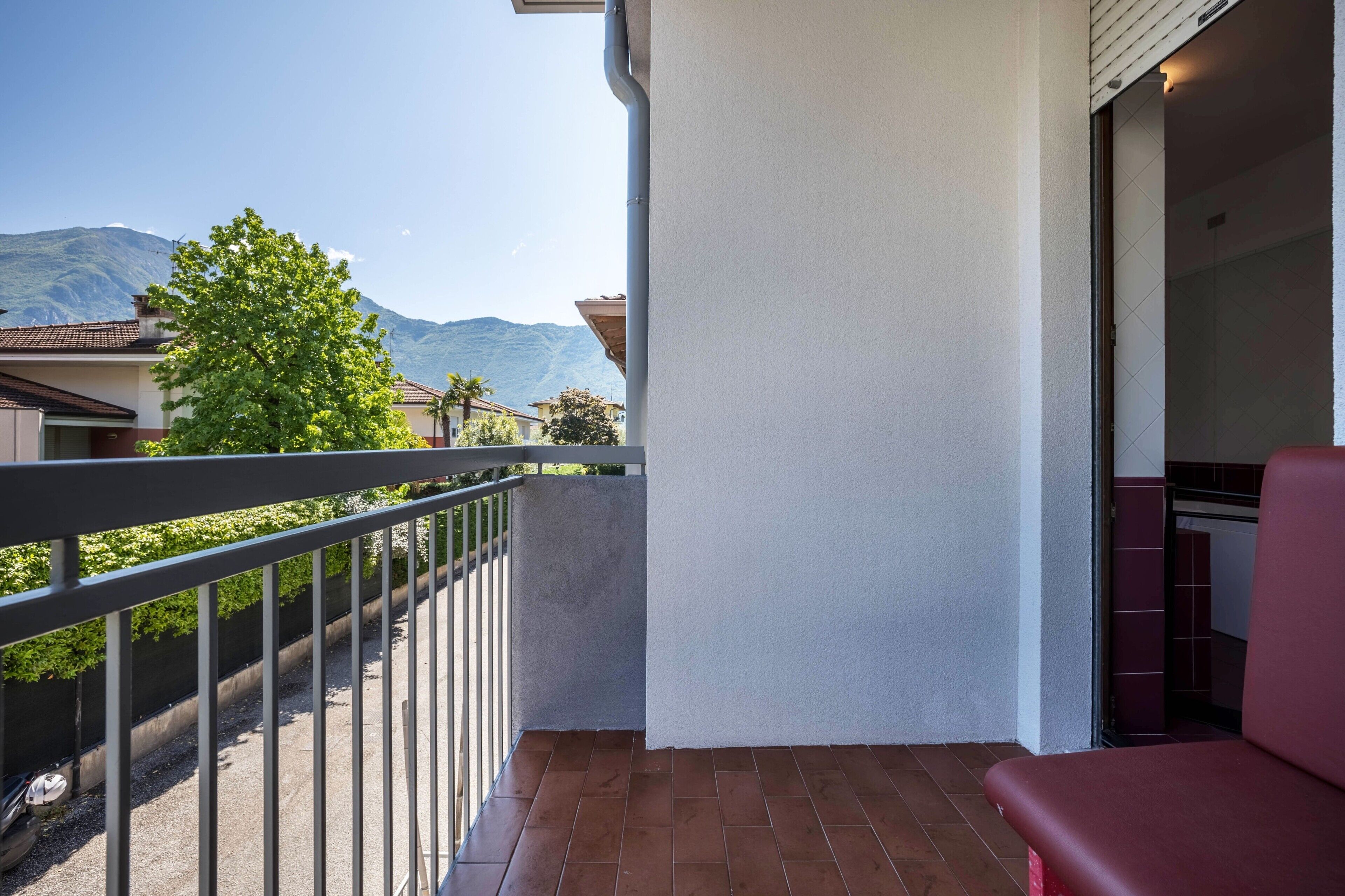 A balcony with a metal railing, a red chair, and a view of mountains and greenery.
