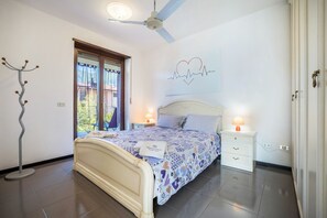 Een slaapkamer met een bed, nachtkastjes, een plafondventilator, een raam met gordijnen en een kunstwerk aan de muur.