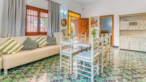 Una sala de estar con sofá, mesa de comedor, sillas, piso estampado, una puerta de madera y un armario.