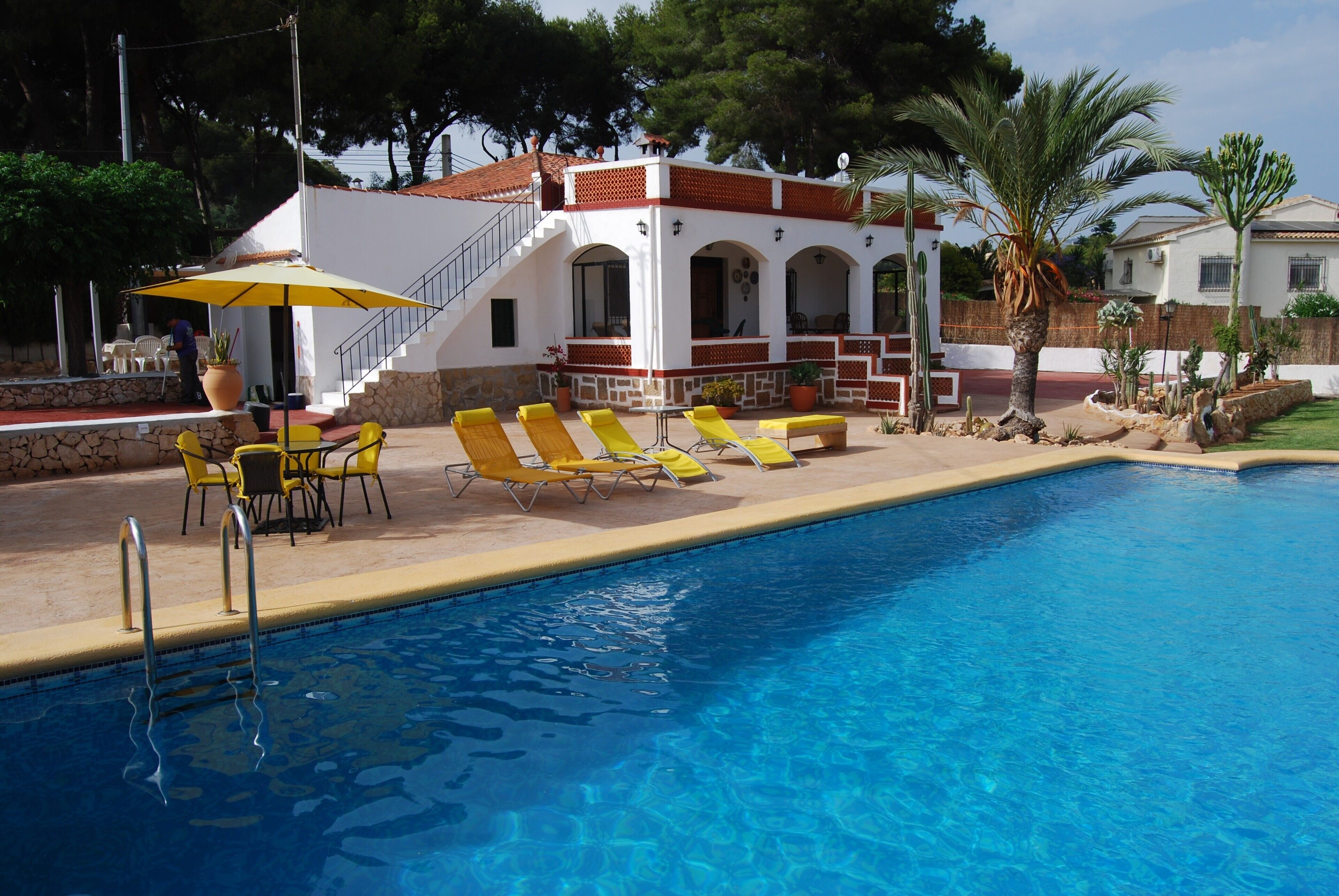 A swimming pool with yellow lounge chairs and a covered seating area with a table and chairs.