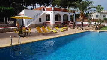 A swimming pool with yellow lounge chairs and a covered seating area with a table and chairs.